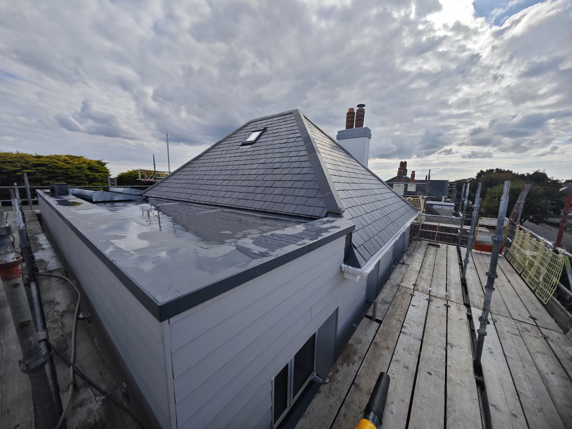 SikaPlan warm flat roof beside a hipped Spanish slate roof under scaffold, Le Clos